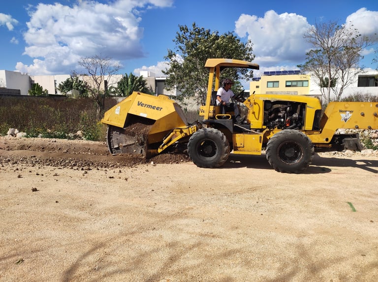 Yellow road roller compactor on construction site with sandy ground and blue sky with clouds