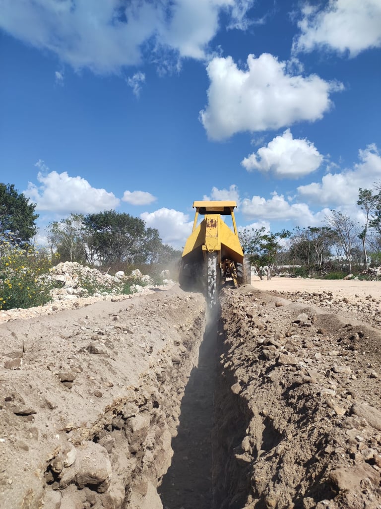 Yellow construction excavator creating a trench in sandy soil under blue sky with white clouds