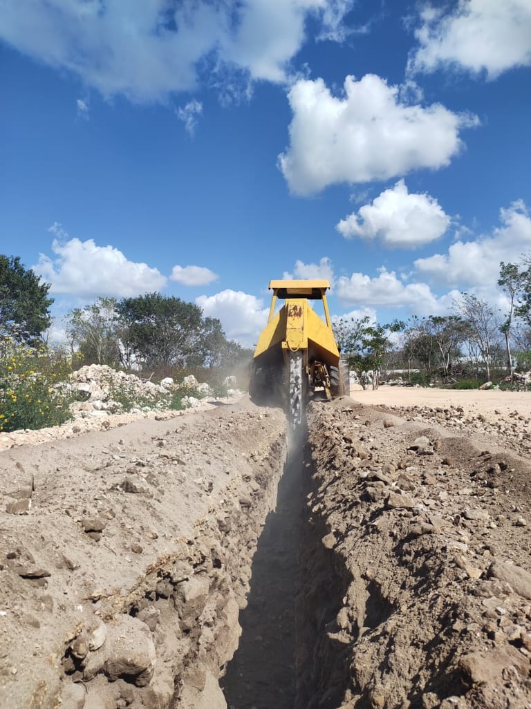 Yellow vibratory roller compacting a trench in sandy soil on a construction site under blue sky