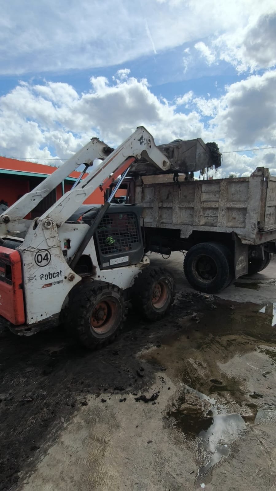 White and red Bobcat telehandler loading gravel into a dump truck on a construction site under blue sky