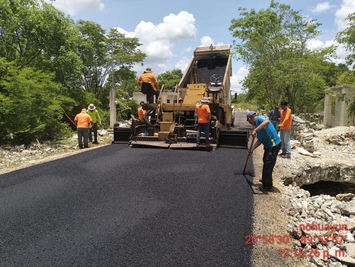 Construction workers in orange vests operating a dump truck to pave a road with asphalt in a rural area
